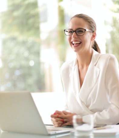 Woman smiling while working on a laptop at a desk in a bright office