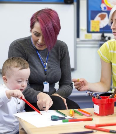 Teacher or Teaching Assistant helping a child with special educational needs draw on a piece of paper in a classroom