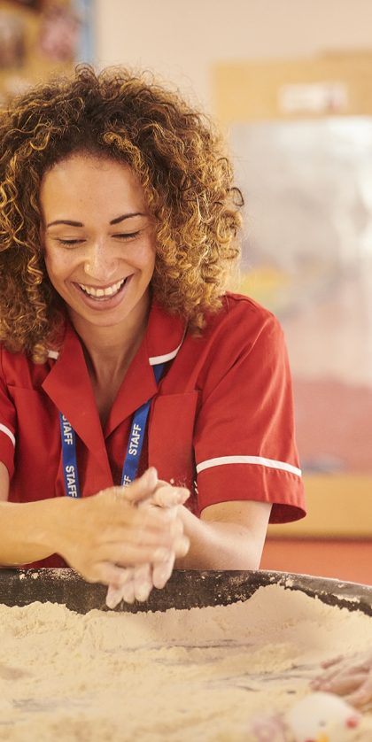Teacher or Teaching Assistant smiling whilst playing in a sand table with a child in a classroom