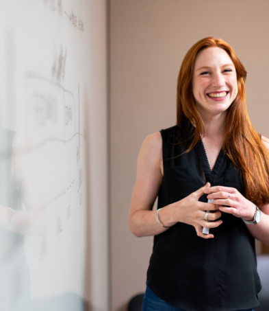 Woman smiling while standing in front of a whiteboard.