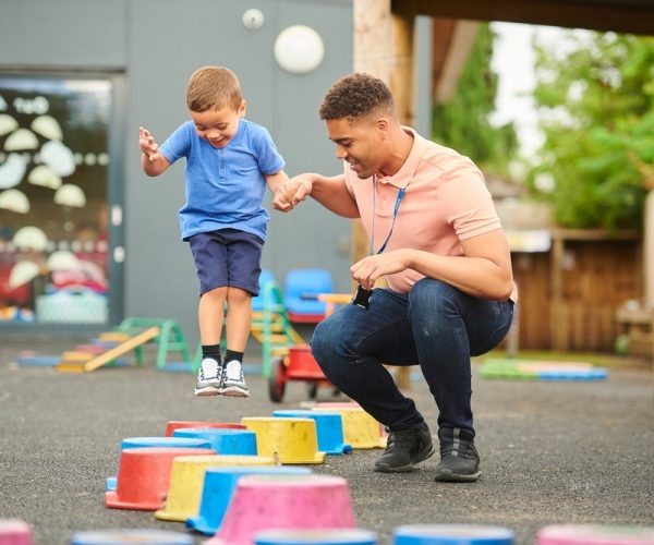 Male nursery worker playing with child who is jumping on blocks