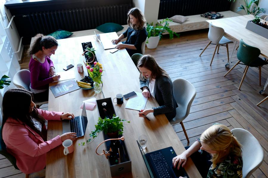 4 jenter som istter sammen rundt et bord og jobber på pc-er