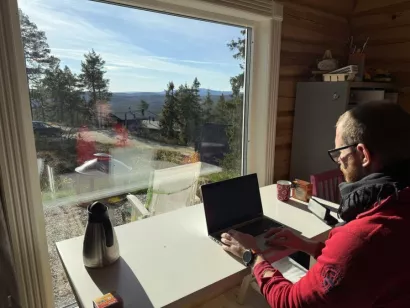 mann sitter på hytta med laptop med utsikt