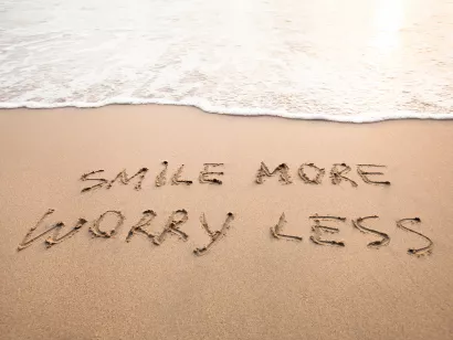 "smile more worry less" skrevet i sanden på strand