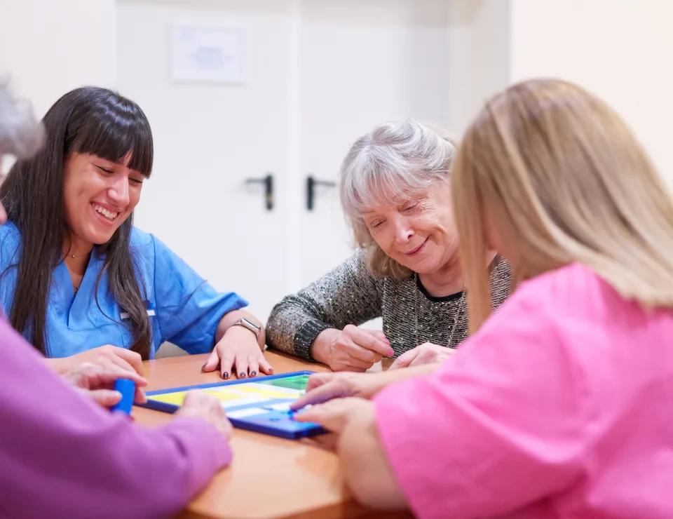 Caregivers and senior women playing a board game, laughing and socializing in a residential care facility