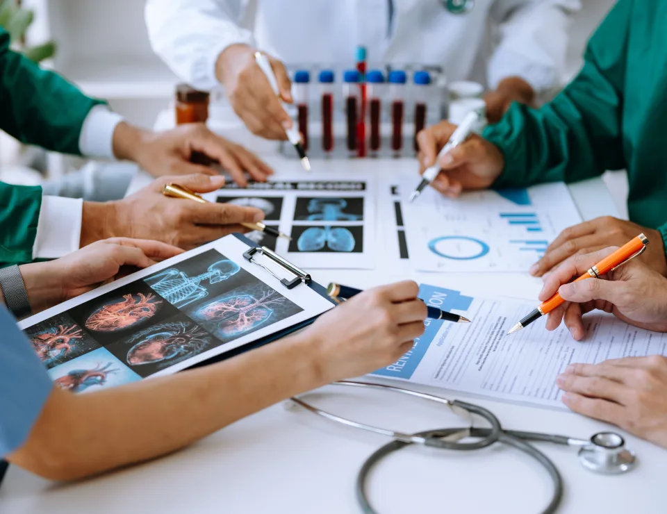 Medical team having a meeting with doctors in white lab coats and surgical scrubs seated at a table discussing a patients working online using computers in the medical industry