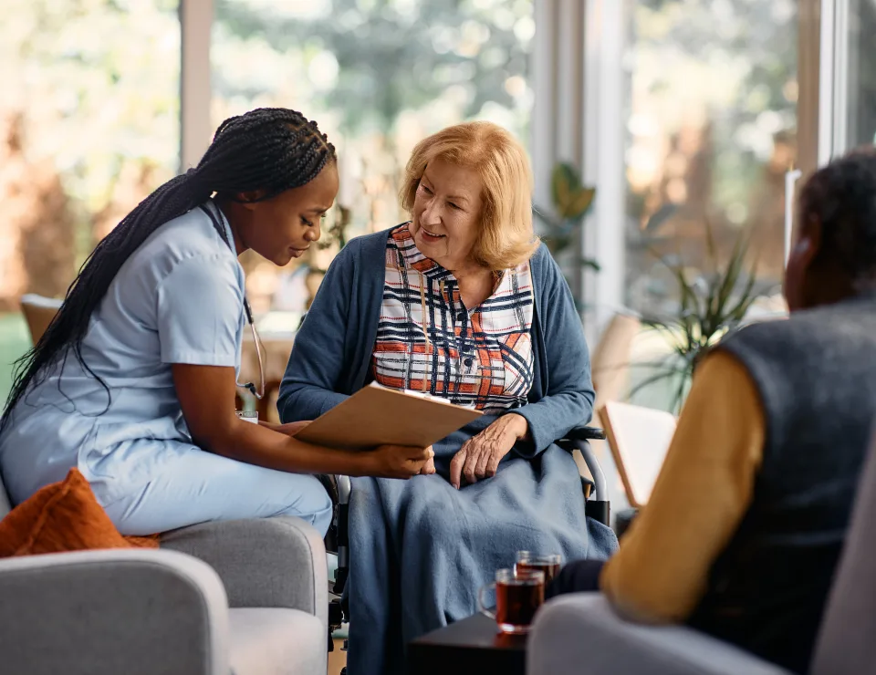 African American nurse analyzing senior woman's medical record while talking to her at nursing home.