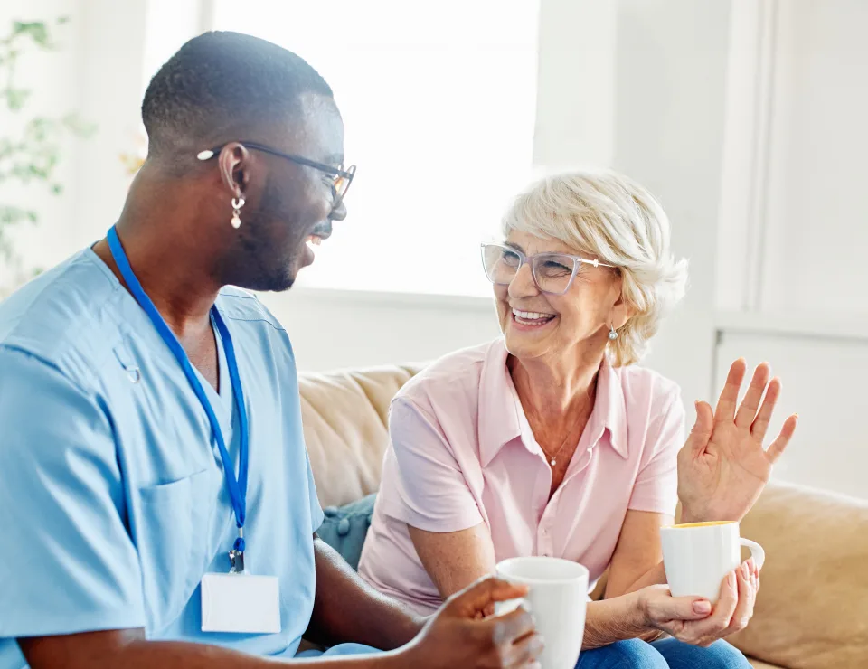 Doctor or nurse caregiver with senior woman drinking tea or coffee at home or nursing home
