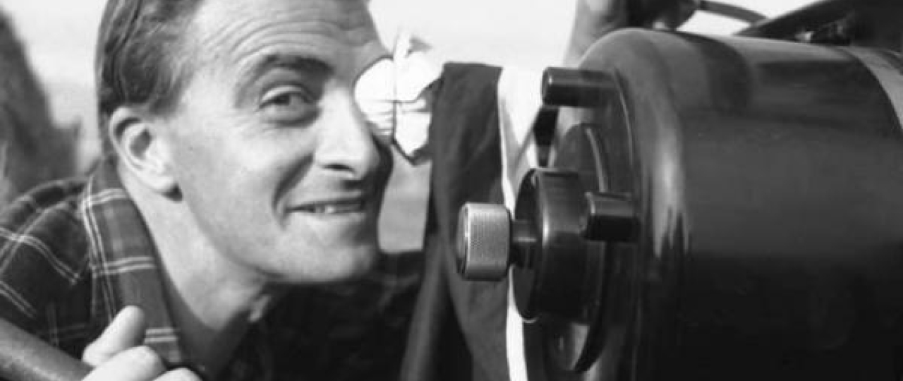 Black and white image of filmmaker Guiseppe de Santis smiling from behind the camera..