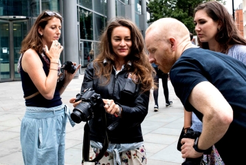 A group of four people on a photography course. One person is showing their camera to another student, who is looking at the photo.