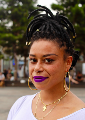 Image a woman with dreadlocks, gold jewelry and purple lipstick.