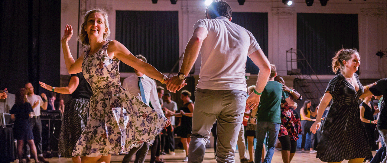 Image of Swing dancers in motion in the Great Hall. The woman is in a dress and the man in a grey t-shirt and jeans.
