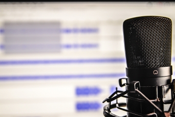 A podcast microphone is in focus, with the back of the image being audio editing software.
