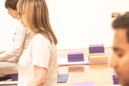 A photo from a Iyengar yoga session at Bishopsgate Institute. The students are sitting crossed legged with their eyes closed and hands on their knees.