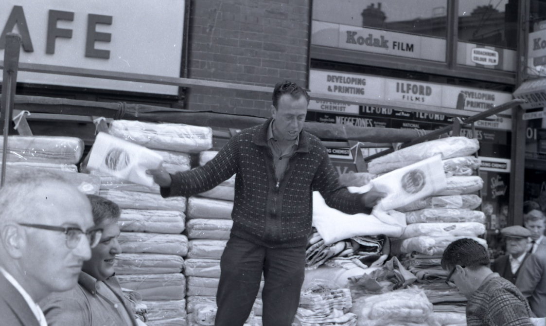 A photo taken on Leather Lane in the early 1960s. He is standing on a box as people walk around him.