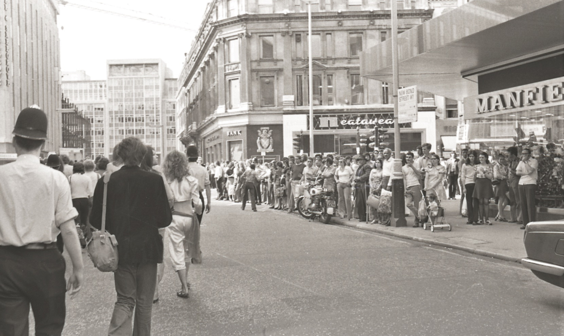 A picture from the second Pride march in 1973. Marchers are walking down the road, with police officers with them.
