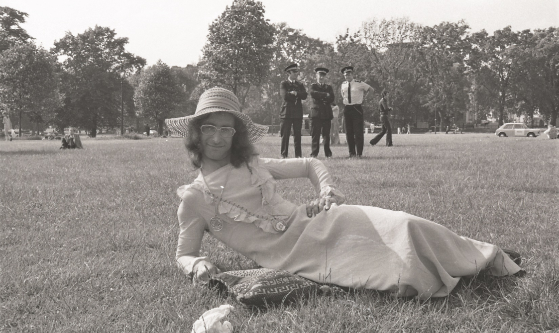 A picture from the second Pride march in 1973. This photo is of someone lying on the grass in Hyde Park wearing a dress and sunhat.