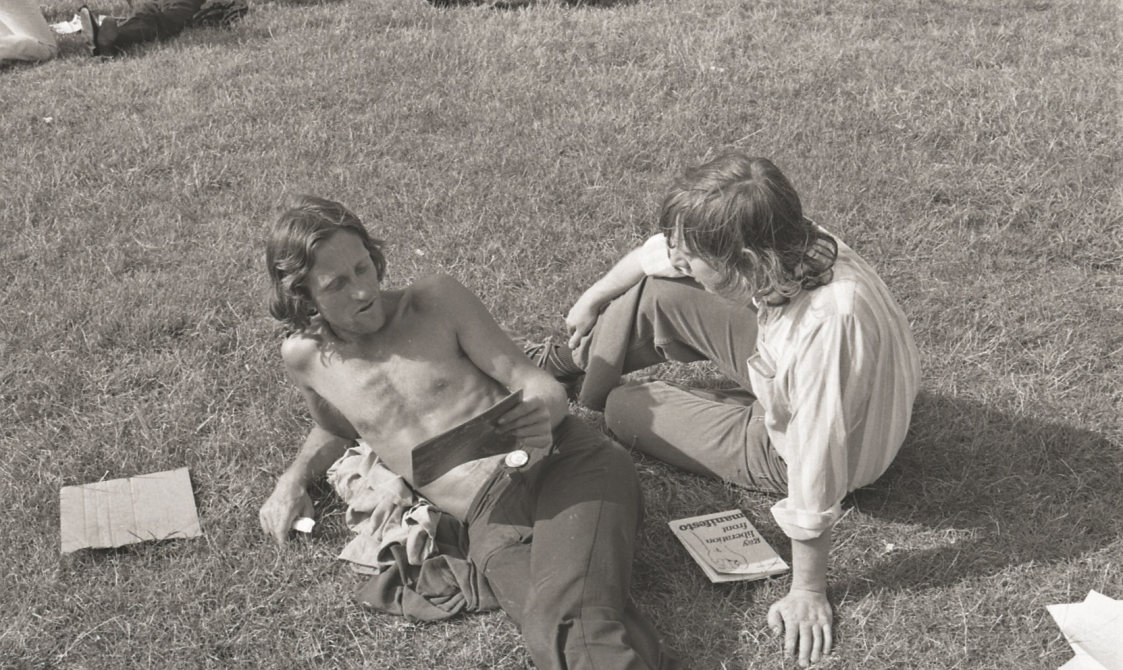 A picture from the second Pride march in 1973. Two people are sitting on the grass in Hyde Park, reading.