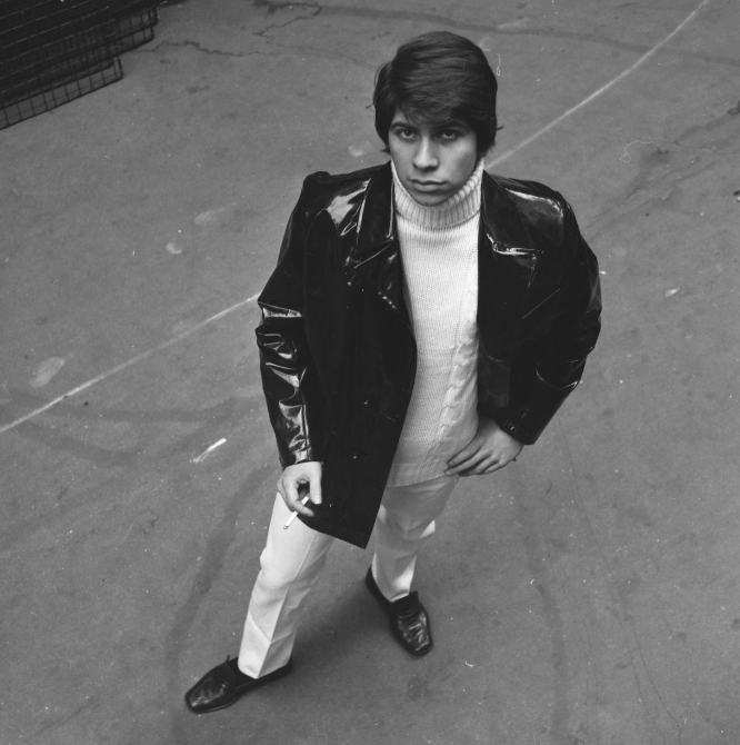 An image taken on Carnaby Street in 1966 of a man wearing white trousers, a white turtleneck, and a leather jacket.