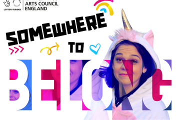 A poster with the words "Somewhere to belong". There is also a young person wearing a unicorn onesie, with a hood.
