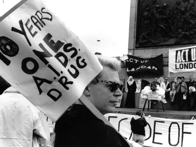A man with sunglasses holding up a placard saying '10 Years one A.I.D.S. Drug'