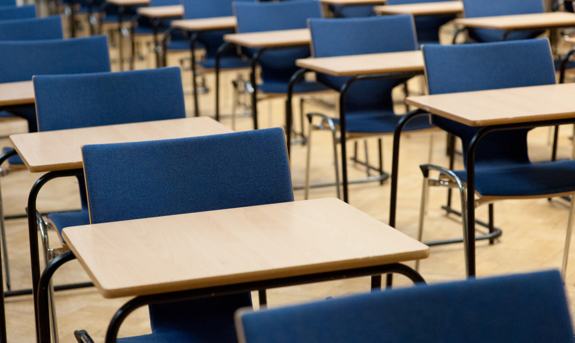 A photograph of exams taking place in the Great Hall. There are rows of single desks with blue chairs behind each desk.