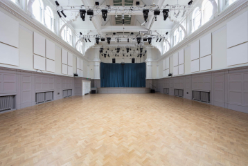 Bishopsgate Institute's Great Hall. There is a stage at the top of the room with blue curtains.