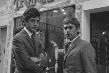Black and white photo from the 1960s of two young men dressed in suits, with similar mod haircuts, looking stern. They are stood outside a clothing shop called Tre Camp.
