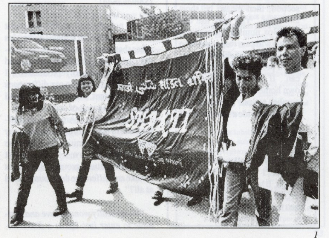 Black and white photo of people marching, holding a large Shakti banner