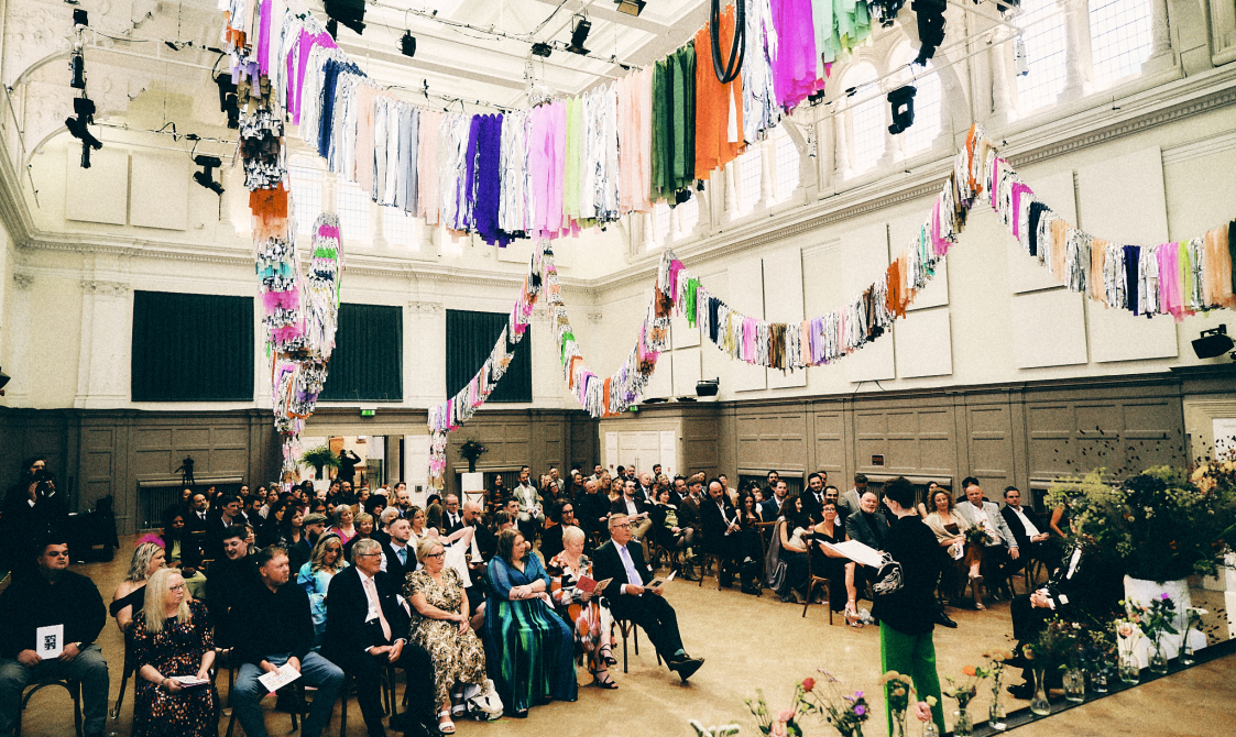 A wedding taking place in a large, high-ceilinged hall decorated with colourful fabrics.