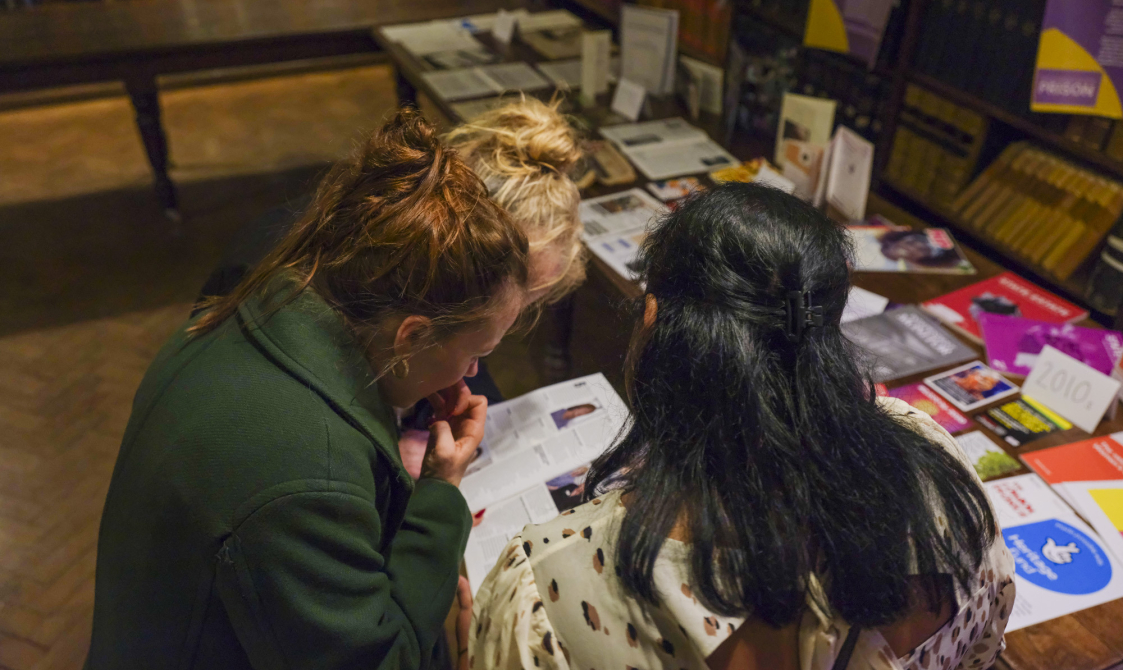 A group of people look at documents and books on a table.