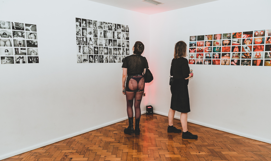 Two people looking at a display o photographs from the Kink and Fetish archives.