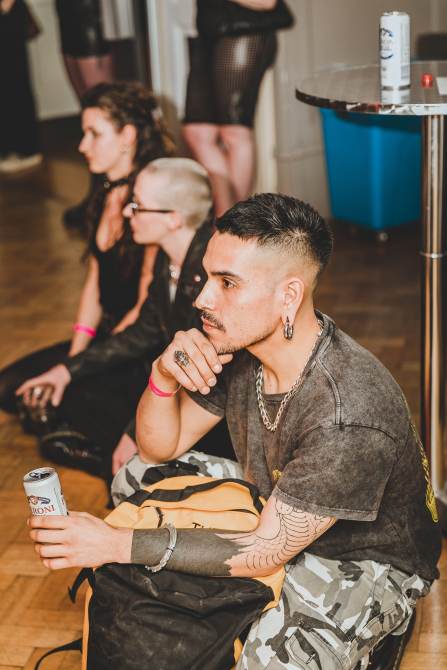 Three people sitting on the wooden floor of the Great Hall. They are watching something to the left of the image.
