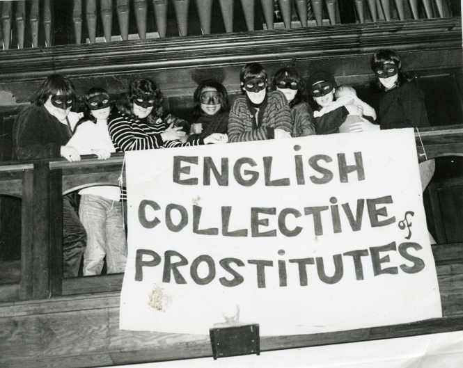 A group of masked sex workers unfurl a banner over the balcony of a church that says "English Collection of prostitutes"