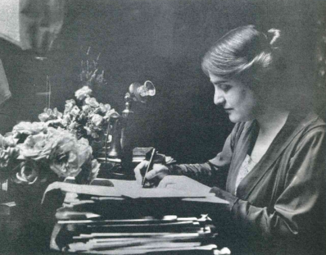 Black and white image of Myra Hess writing at her desk.