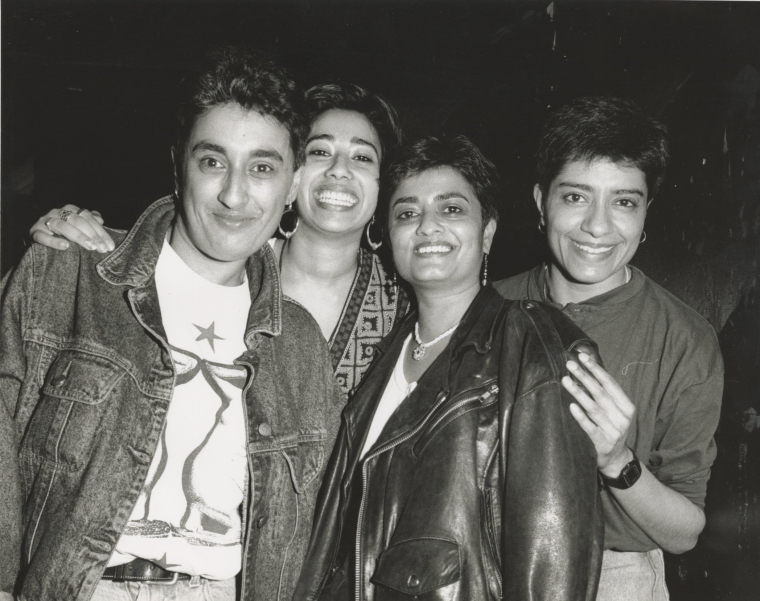 A black and white picture of four South Asian women looking at the camera and smiling