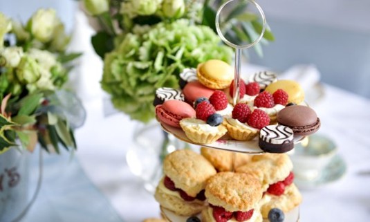 A table with cakes and sandwiches and a glass of wine 