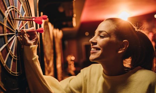 woman pulling darts out of a dart board smiling