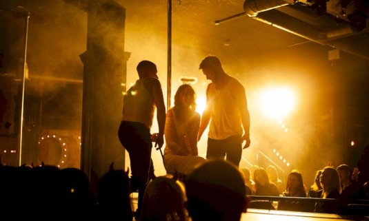 Woman sitting down on stage with 2 dreamboys on either side