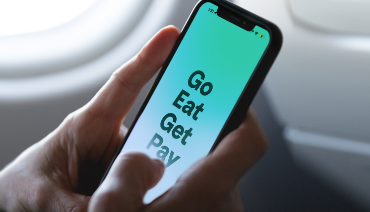Close-up of a person holding a smartphone displaying a screen with the words 'Go, Eat, Get, Pay' in bold text on a gradient background, likely promoting an all-in-one lifestyle or super app