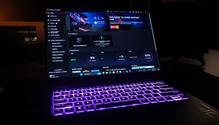 A close-up view of an open HP Omen Transcend 14 laptop in a dimly lit room, focusing on its screen which displays the "OMEN Gaming Hub" software. The screen shows various system metrics like CPU utilization (9%), GPU data, RAM (50%), and temperature (56°C). The laptop's keyboard is illuminated with a bright purple light.
