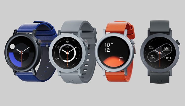 A lineup of four CMF Watch Pro 2 smartwatches, each with a round black display and distinct band and bezel colors, arranged on a light grey background. From left to right: a watch with a black bezel and a dark blue band, a watch with a silver bezel and a light grey band, a watch with a silver bezel and a bright orange band, and a watch with a dark grey bezel and a matching dark grey band. Each watch face displays different digital or analog time and fitness information.