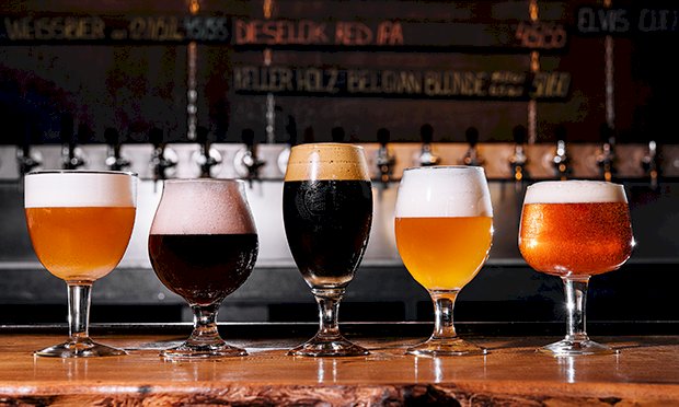 Four glasses of beer on a bar.