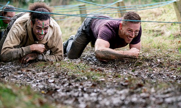 Two men crawling through a muddy assault course.