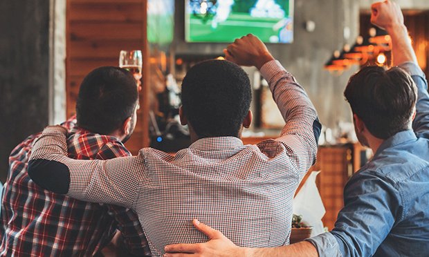 three men in a bar watching sport with beers