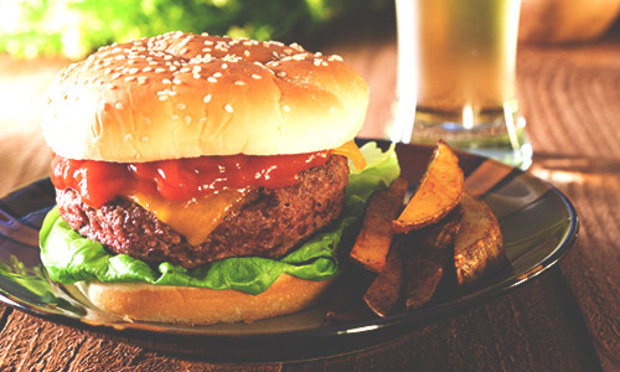 Crispy chips lying next to a burger piled high with lettuce, cheese and red sauce on a sesame seed bun. Explore the Lincoln 2 Course Meal for your stag weekend: