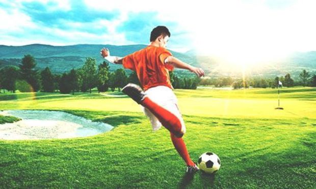 Guy on a golf course in the mountains kicking a football towards a tee. Discover the Lincoln Footgolf stag party experience: