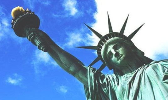 Daytime photo of the Statue of Liberty with the sky slightly cloudy and deep blue. Explore New York Stag Party ideas below: