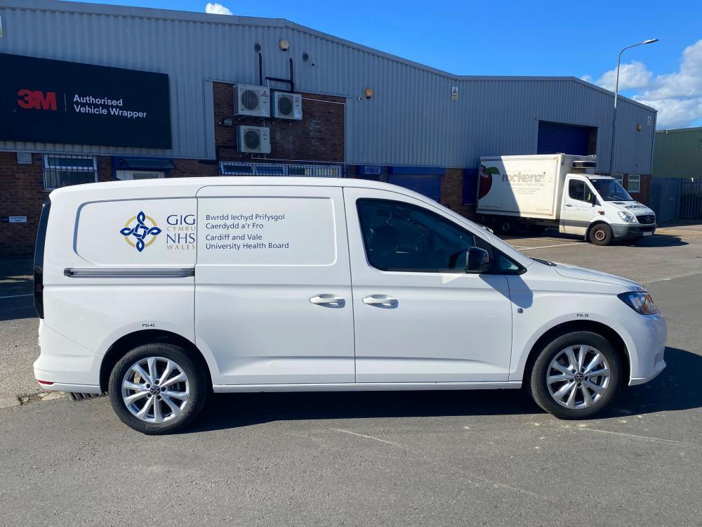 White Volkswagen Caddy van with NHS branded vinyl graphics outside Popin vehicle wrap centre in Cardiff.