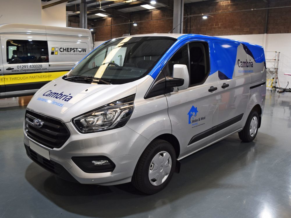 Partial vehicle wrap with graphics on silver company Ford Transit Custom van.